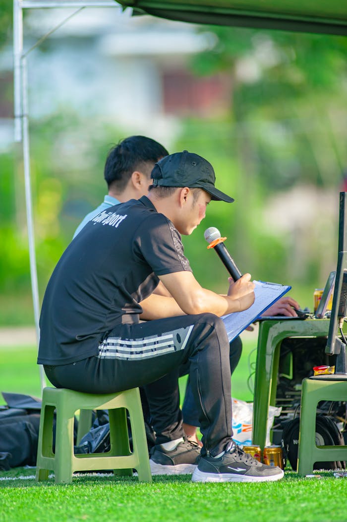 gallery-02 Two men managing a sports event in Hanoi, using a microphone and laptop outdoors.