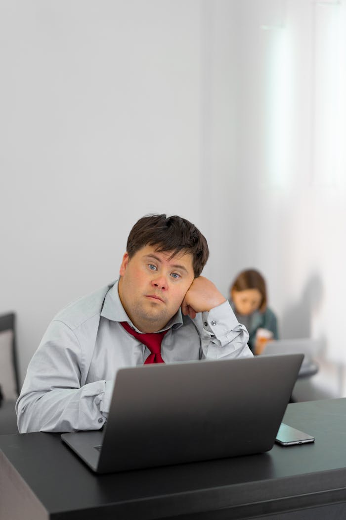 gallery-05 A man with Down syndrome sitting at a desk using a laptop in an office setting.